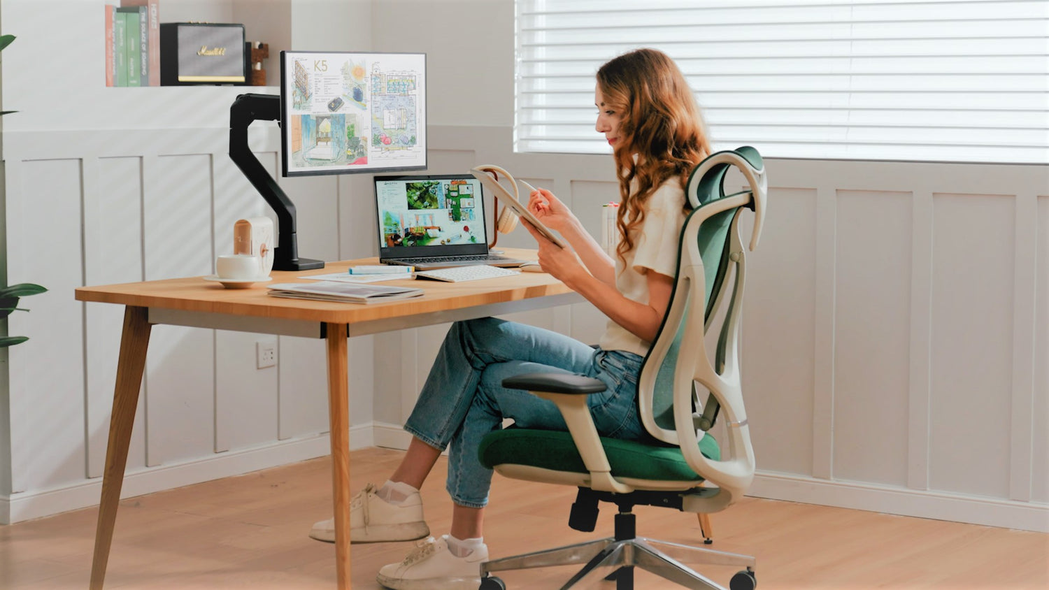 Woman working at a desk with tablet, laptop, and monitor mounted on a monTEK arm in a bright home office